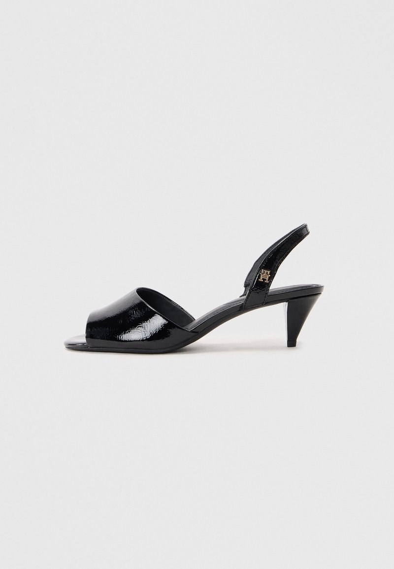 Chaussure slingback en cuir verni noir à bout ouvert, talon effilé de hauteur moyenne et détail logo doré sur la bride.