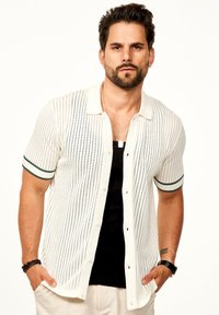 Strickhemd mit kurzen Ärmeln in Creme mit einem perforierten Design, ausgestattet mit einem Kragen und dunkelgrünen Akzenten an den Ärmeln.