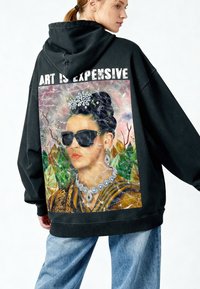 Hoodie noir oversize avec un graphisme vif d'une femme parée de bijoux, accompagné du texte "L'ART EST CHER" au-dessus de l'image.
