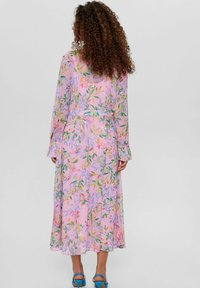 Robe longue rose avec un motif floral vert et multicolore, en tissu transparent, à manches longues, taille ajustée, jupe fluide et léger éclat.