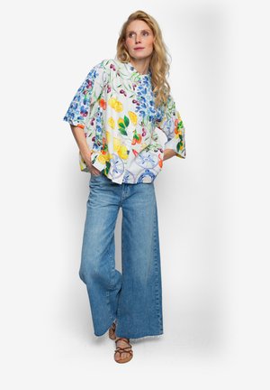 Mehrfarbige Bluse mit Blumen- und Fruchtmustern, die eine lockere Passform und breite Ärmel aufweist. Kombiniert mit hoch taillierten, hellblauen Jeans mit weitem Bein.