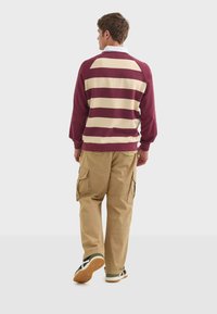 Mørkebrun og creme-stribet pullover med hvid krave, parret med lysebrune cargo-bukser. Tekstureret stof med droppet skulderdesign og ribbede manchetter.