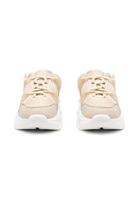 Zapatillas deportivas beige con parte superior de tela texturizada, suela de goma blanca y bandas elásticas contrastantes; presentan una puntera redondeada y cierre de cordones.