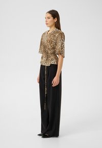 Leopard print top with short sleeves and a drawstring waist, paired with wide black trousers and pointed black shoes. Smooth fabric texture.