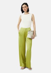 Biała prążkowana bezrękawnik, wysokosiedzące satynowe zielone spodnie szerokie nogawki, trzymająca małą jasnoszara torebkę oraz nosząca białe sandały na otwartym palcu.