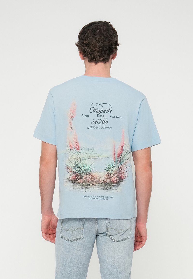 Ανοιχτό μπλε βαμβακερό t-shirt με γραφικό σχέδιο στην πλάτη που απεικονίζει στυλιζαρισμένα φυτά και κείμενο. Με κοντά μανίκια και στρογγυλή λαιμόκοψη.