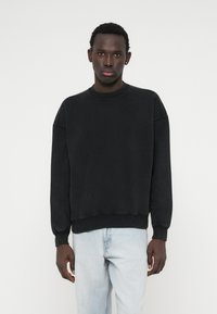 Černá mikina s kulatým výstřihem, voln�ým střihem, dlouhými rukávy a žebrovanými manžetami. Kombinováno se světle modrými džíny, minimalistický design.