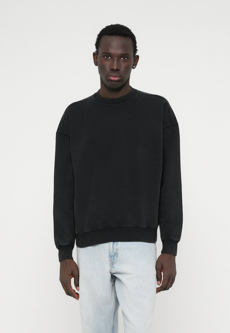 Černá mikina s kulatým výstřihem, volným střihem, dlouhými rukávy a žebrovanými manžetami. Kombinováno se světle modrými džíny, minimalistický design.