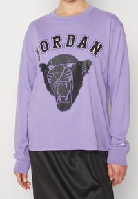 Violetti pitkähihaineen collegepaita, jossa on musta grafiikka kiljuvasta pantterista ja "JORDAN"-teksti yläpuolella. Pehmeää puuvillamateriaalia ja rento leikkaus.