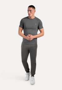 Grijze sportshirt met korte mouwen en ronde hals, gecombineerd met bijpassende grijze joggingbroek en witte sneakers. Slank, strak design.