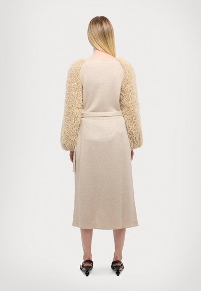 Beiges Strickkleid mit weichen, flauschigen cremfarbenen Ärmeln. Figurbetonter Oberkörper und Taillengurt, knielange Länge, glatte Textur mit subtiler Eleganz.
