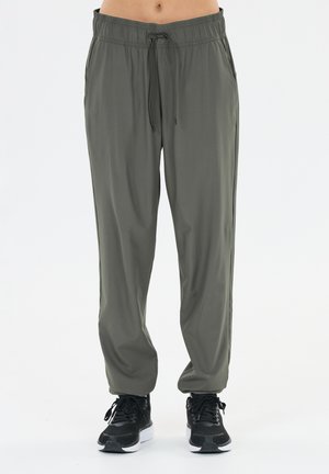 Olivegrüne Hose mit geradem Bein und Kordelzug in der Taille, getragen mit schwarzen Sportschuhen an einer stehenden Person.