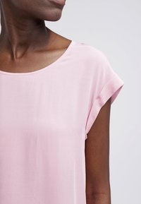 Top rosa chiaro a maniche corte con scollatura rotonda. Realizzato in tessuto morbido, presenta una vestibilità comoda e polsini delle maniche arrotolati.