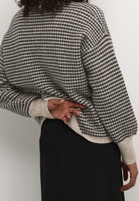 Grau- und cremefarbener gestrickter Pullover mit gepunktetem Muster, überschnittenen Schultern und gerippten Bündchen, getragen über einem schwarzen Kleidungsstück.