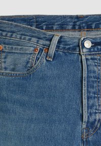 Jeans in denim blu con un design classico, caratterizzati da rivetti in rame, chiusura frontale a pulsante e dettagli di cucitura prominenti.
