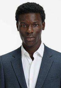 Blazer blu scuro con trama e rever con intaglio, abbinato a una camicia bianca elegante. Presenta una tasca sul petto e linee pulite.