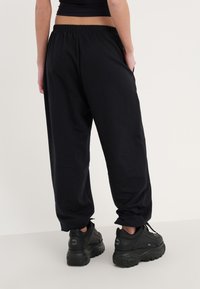 Pantalon de survêtement noir avec une taille élastique, des poignets fuselés et des poches latérales, associé à des baskets noires chunky.
