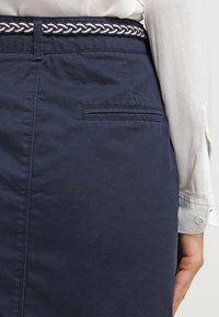 Námořnická modrá sukně s tkaným opaskem s béžovým lemem, hladkou texturou, zadní kapsou a upraveným střihem pro těsně přiléhající vzhled.