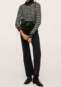 Pull à carreaux noirs et blancs avec un col montant et des poignets côtelés, associé à un jean noir taille haute et des bottines à talons noires.