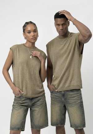 To modeller iført matchende olivengrønne ærmeløse toppe og falmede denimshorts poserer mod en ensartet hvid baggrund.