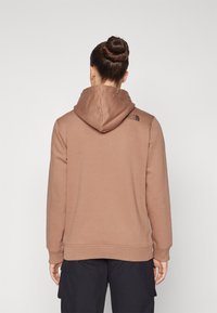 Felpa marrone realizzata in tessuto morbido, con cappuccio, polsini a coste e un piccolo logo sulla parte superiore della schiena. Design semplice, senza motivi visibili.