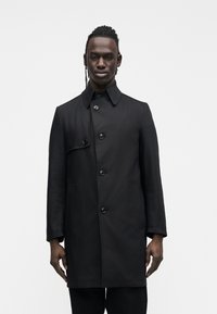 Czarny, płaszcz o długości do połowy uda, z zapięciem na guziki, ostrym kołnierzem i dwoma bocznymi kieszeniami. Gładka faktura z minimalistycznymi elementami designu.