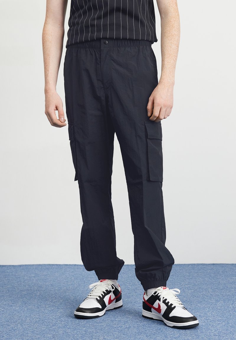 Svarta cargo-byxor med elastisk midja, med sidofickor och ett lätt, texturerat tyg. Matchas med svarta och vita sneakers.