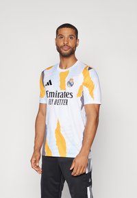 Maglietta bianca a maniche corte con motivi astratti arancioni, blu e grigi. Presenta il logo "Emirates Fly Better" e le strisce Adidas sulle maniche.