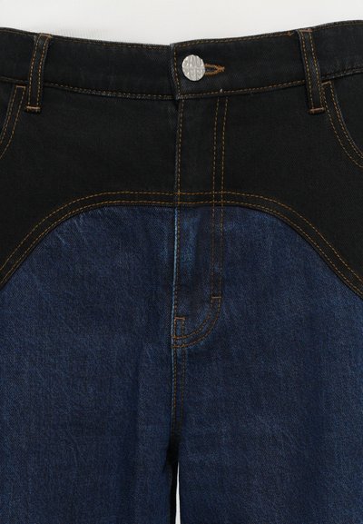 Must mustra ja tumesinised teksapüksid, millel on kontrastsed kangas osad, kollased õmblused ja hõbedane nööp sulgemisel.