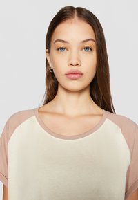 Kortärmad t-shirt med en krämfärgad kropp och ljusrosa raglanärmar. Mjuk tyg med en slät textur och rundad halsringning.