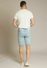 Shorts en denim bleu clair à coupe slim, dotés de poches arrière et d'une texture délavée, associés à un t-shirt blanc uni à manches courtes.