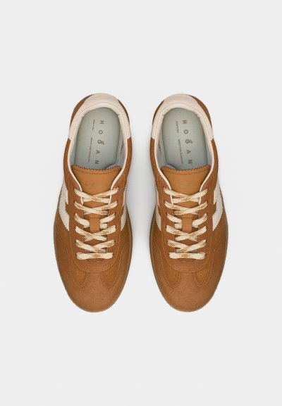 Ζευγάρι καφέ σουέντ αθλητικά παπούτσια με κρεμ κορδόνια και λευκές πλευρικές ρίγες, σε θέα από πάνω σε ανοιχτό γκρι φόντο.