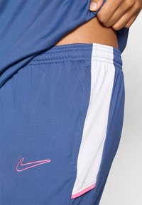 Αθλητικό σορτς Nike με μονόχρωμο μπλε ύφασμα με υφή, λευκή πλαϊνή πινακίδα και ροζ κεντημένο λογότυπο μπροστά.