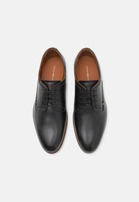 Chaussures habillées en cuir noir avec une finition lisse, bout rond, design à lacets, et une doublure intérieure marron affichant le nom de la marque.