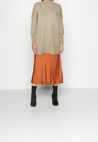 Top lavorato a maglia beige a coste con spalle scese, abbinato a una gonna midi in satin color ruggine e stivaletti neri alla caviglia. Silhouette semplice e moderna.