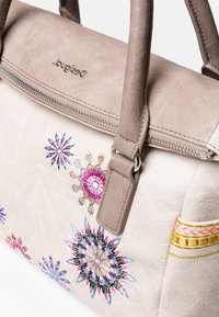 Beżowa syntetyczna torebka z wielokolorowym haftem kwiatowym, z podwójnymi uchwytami na górze i zamkiem błyskawicznym. Gładka tekstura z ozdobnym szyciem.