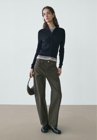 Navy ribbed zip-up sweater, grey t-shirt, olive green wide-leg pants, black boots, and a small brown handbag. Simple, modern design.