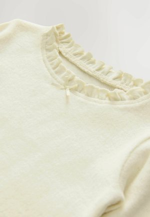 Cremfarbener Oberteil aus weichem Stoff. Verfügt über einen Rüschenausschnitt und ein kleines Bandakzent am Kragen. Einfache und strukturierte Oberfläche.
