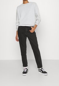 Felpa grigia chiara, jeans neri e sneakers Vans nere con dettagli bianchi. Look informale con polsini e vita a coste.
