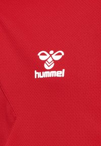 Rød sportstrøje lavet af åndbart stof; har en struktureret overflade og et hvidt "hummel" logo med et bierdesign.