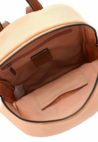 Sac à dos en nylon rose avec une tirette en cuir marron, présentant un intérieur spacieux, une poche latérale et une texture lisse. Ouverture zippée.