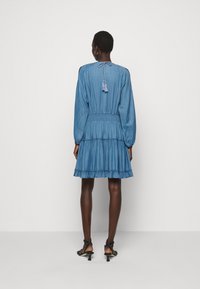 Jeansmekko vaaleansinisessä värissä, jossa on pitkät hihat, röyhelöhelma, joustava vyötärö ja takana nauhakoristelu. Sileä pinta ja rento istuvuus.