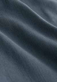 Sötétkék bordázott szövet lágy, texturált felülettel, finom hullámokkal és redőkkel, amelyek kiemelik az anyag összetételét.