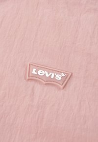 Το ροζ ύφασμα της Levi's με υφή περιλαμβάνει λευκό, ανάγλυφο λογότυπο "Levi's" σε αντίθετο ανοιχτό ροζ πλαίσιο.
