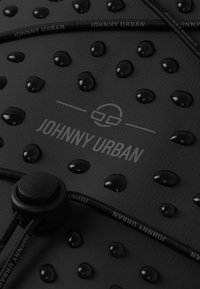 Fekete vízálló felület, kiemelkedő cseppekkel, rajta szürke "JOHNNY URBAN" logóval és húzózsinóros rögzítési megoldással.