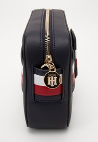 Marineblauwe leren cosmeticazak met gouden rits en hardware. Bevat rode en witte horizontale strepen en een logo pendant.