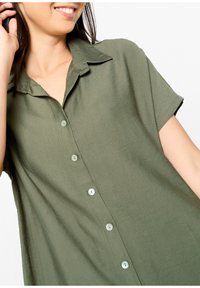 Koszula z krótkim rękawem w oliwkowym kolorze, wykonana z lekkiego materiału, z kołnierzykiem, z jasnymi guzikami z przodu.