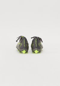 Botas de fútbol grises con un upper texturizado, acentos verdes vibrantes y un diseño aerodinámico. Los cordones están atados en la parte trasera; los tacos son visibles.