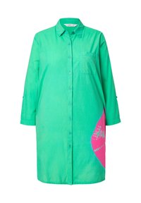 Chemise verte à manches trois-quarts, ornée d'un motif abstrait rose d'un côté et d'une poche sur la poitrine. Tissu au toucher doux.