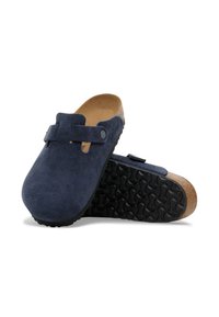 Sabots en suède bleu marine avec une semelle intermédiaire en liège, une sangle ajustable et une semelle extérieure en caoutchouc texturé. Doublure intérieure lisse pour le confort.